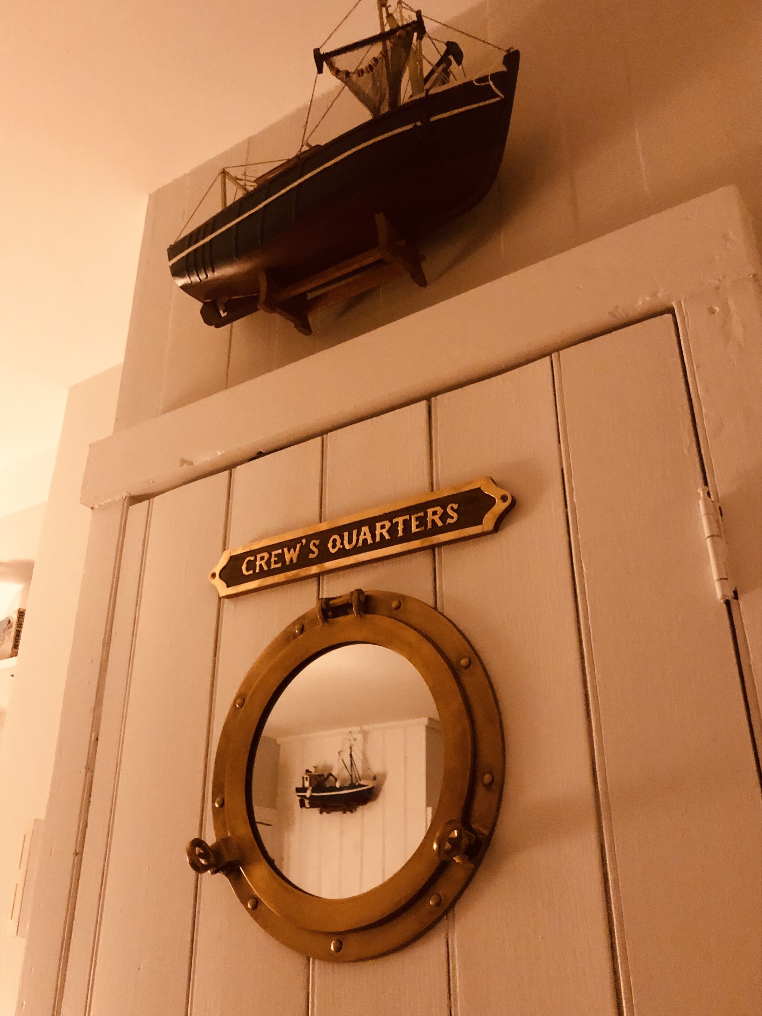 A door with a brass porthole and a sign reading "CREW'S QUARTERS".