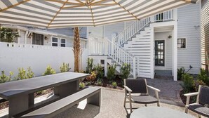 A covered patio with a table and chairs, a staircase, and a white building in the background. - Cozy Charleston Fall Stay | 3BR + Shared Backyard (Charleston)