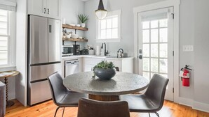 A modern kitchen with white cabinetry, a stainless steel refrigerator, a round table with chairs, and a pendant light. - Cozy Charleston Fall Stay | 3BR + Shared Backyard (Charleston)