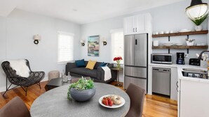 A modern kitchen with a refrigerator, microwave, and coffee maker. There is a dining table with a bowl of fruit and a vase of flowers. - Cozy Charleston Fall Stay | 3BR + Shared Backyard (Charleston)