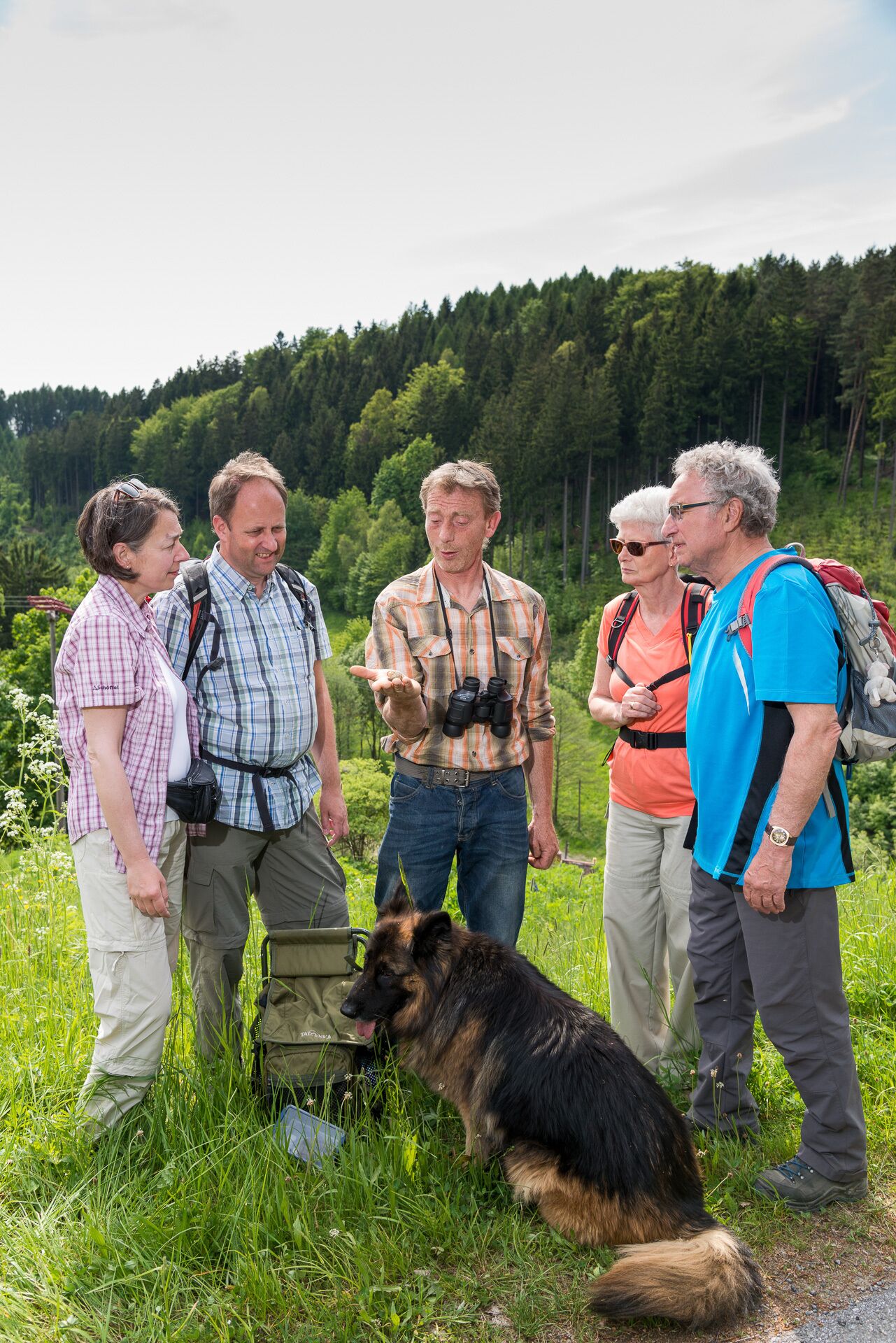 Un grupo de personas de pie en un campo cubierto de hierba, con un perro, rodeado de árboles.