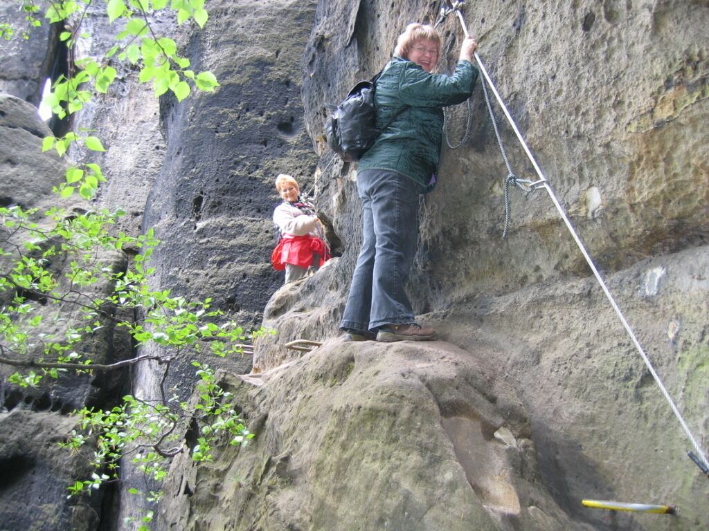 A person climbing a rocky cliff with a rope.