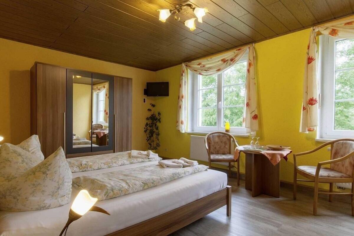 Un dormitorio con una cama grande, un escritorio, dos sillas, un espejo y un televisor.