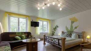 A cozy room with a bed, a sofa, a small table, and a TV mounted on the wall.