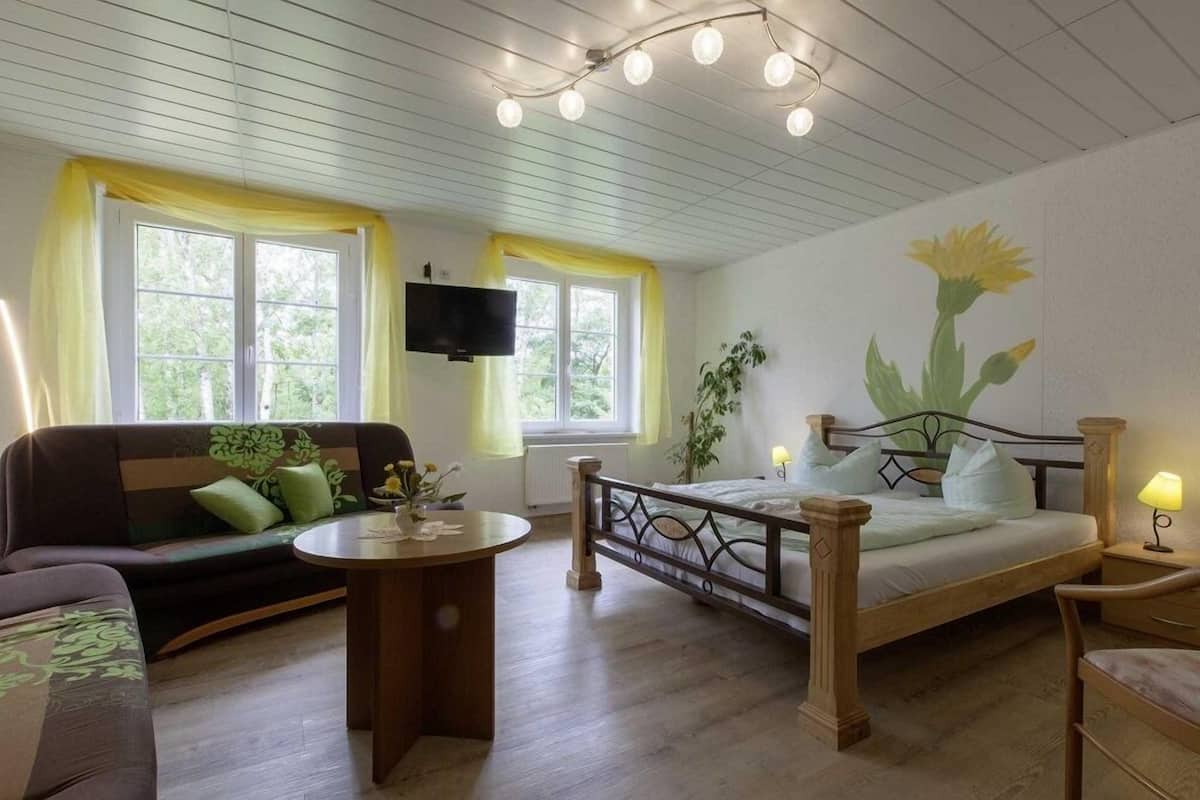 Una habitación acogedora con una cama, un sofá, una mesita y un televisor fijado a la pared.