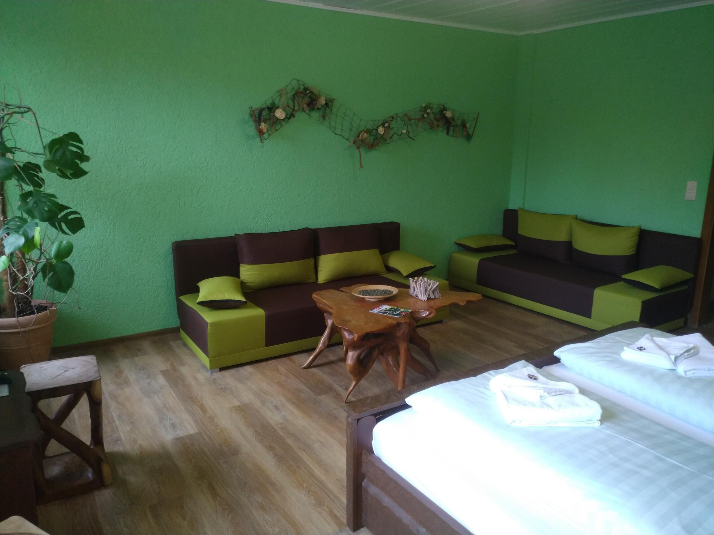 A room with a green wall, a sofa, a wooden table, and a bed.