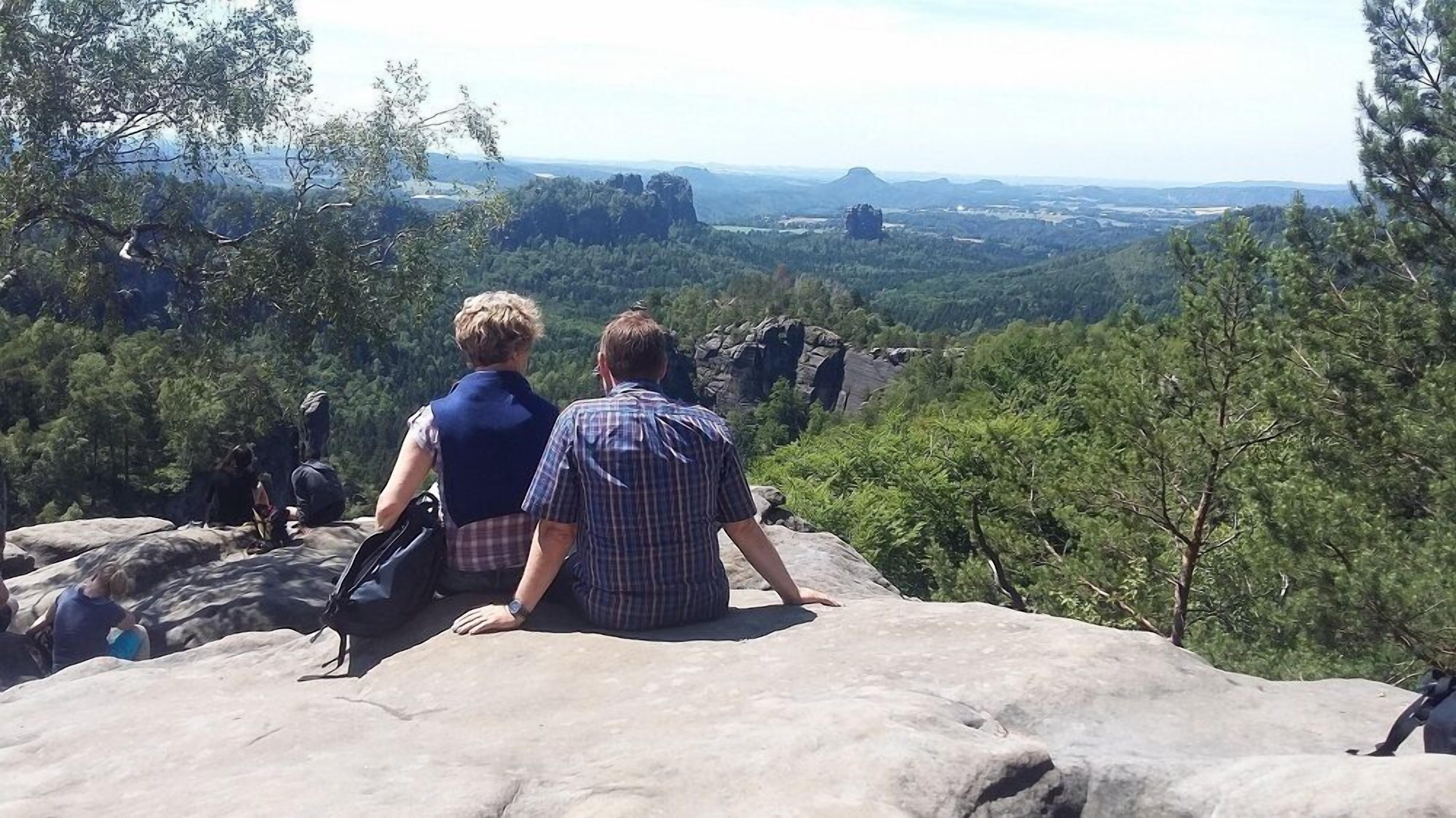 Two people sitting on a rock overlooking a forested valley.