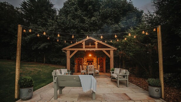 An outdoor patio with a wooden pergola, stone flooring, and string lights. - Rural Holiday Cottage With Log Burner (Buxton)