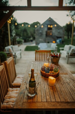 An outdoor wooden table set for dining with a bottle of wine, a candle, and a glass pitcher. - Rural Holiday Cottage With Log Burner (Buxton)