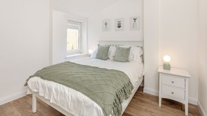 A bedroom with a bed, a bedside table, a window, and wall art.