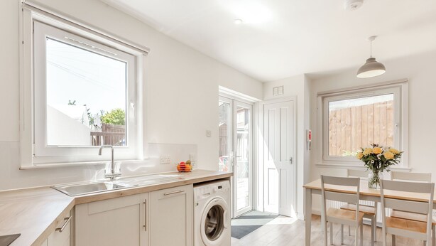 A modern kitchen with a built-in washing machine, a dining area with a table and chairs, and large windows providing natural light.