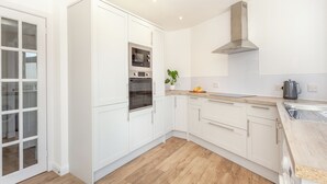 A modern kitchen with white cabinetry, a built-in oven, a stainless steel range hood, and a wooden countertop.