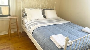 A neatly made bed with a striped bedspread, two pillows, and a folded towel on a white metal frame bed in a room with wooden flooring and a window with blinds. - GREAT UPPER MANHATTAN APARTMENTS FOR GROUP AND FAMILIES (new york)
