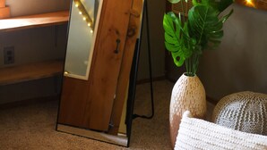A mirror with a wooden frame, a potted plant, and a knitted cushion on a carpeted floor. - Meadow View Cottage (Manheim)