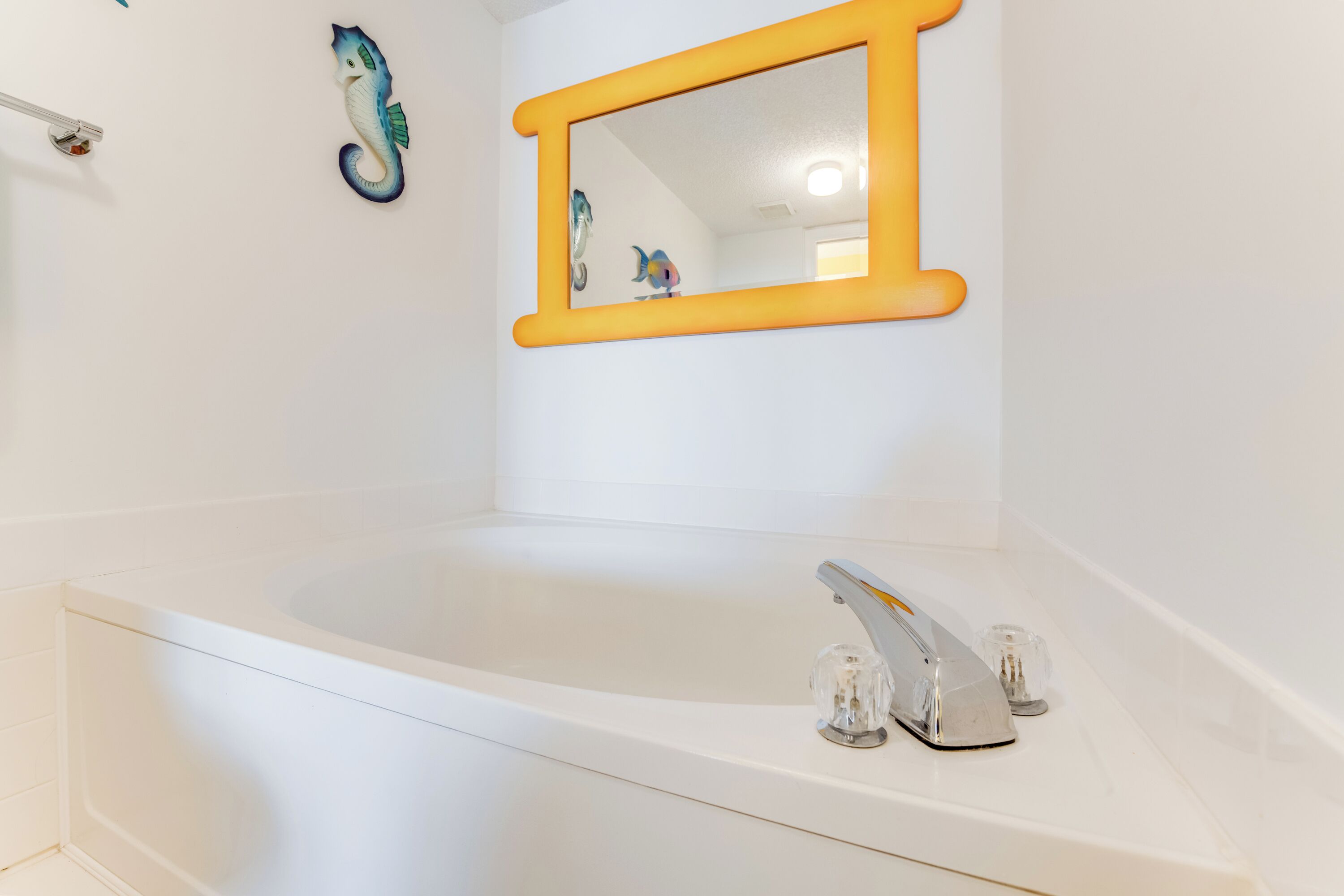 A white bathtub with a modern faucet, a yellow-framed mirror, and a decorative fish sculpture on the wall.