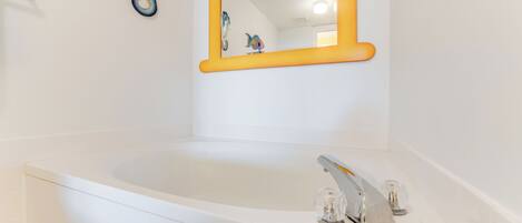 A white bathtub with a modern faucet, a yellow-framed mirror, and a decorative fish sculpture on the wall.