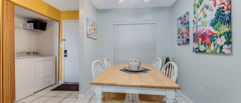A dining area with a wooden table and chairs, a ceiling fan, and two wall-mounted paintings.