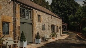 A stone building with a large garage door, a bench, and potted plants on the sidewalk. - Luxury Rural Holiday Cottage With Log Burner (Buxton)