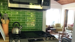 A kitchen with a stainless steel stove, a microwave, and a green tiled backsplash. - Bright and Cheerful Lake Front Beach Cottage (Cedar Grove)