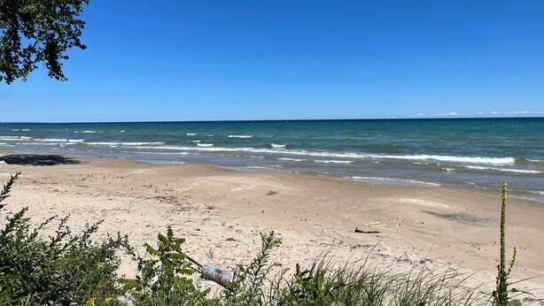 A beach with clear skies and calm waves. - Bright and Cheerful Lake Front Beach Cottage (Cedar Grove)