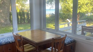 A dining area with a wooden table and chairs, large windows with a view of the outdoors, and a ceiling fan. - Bright and Cheerful Lake Front Beach Cottage (Cedar Grove)