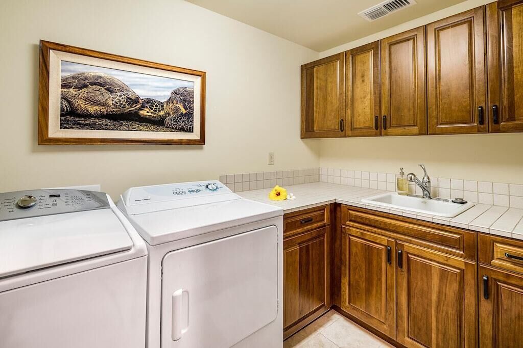 A laundry area with two washing machines, a sink, wooden cabinets, and a framed picture on the wall.