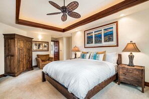 Ein Schlafzimmer mit einem großen Bett, einem Holz-Kopfteil, einem Deckenventilator, einem Holzschrank, einem gerahmten Bild an der Wand und einem Nachttisch mit einer Lampe.