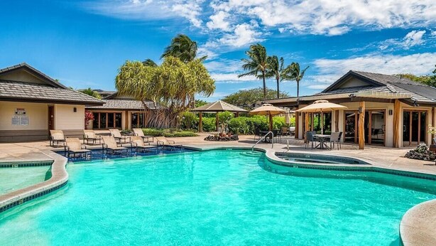 Uma piscina com espreguiçadeiras e guarda-sóis, rodeada por edifícios com decoração tropical.