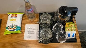 Mesa en una habitación de hotel con una bandeja que contiene una botella de agua, un paquete de aperitivos, una cafetera y un menú.