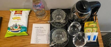 A hotel room table with a tray containing a bottle of water, a packet of snacks, a coffee maker, and a menu.