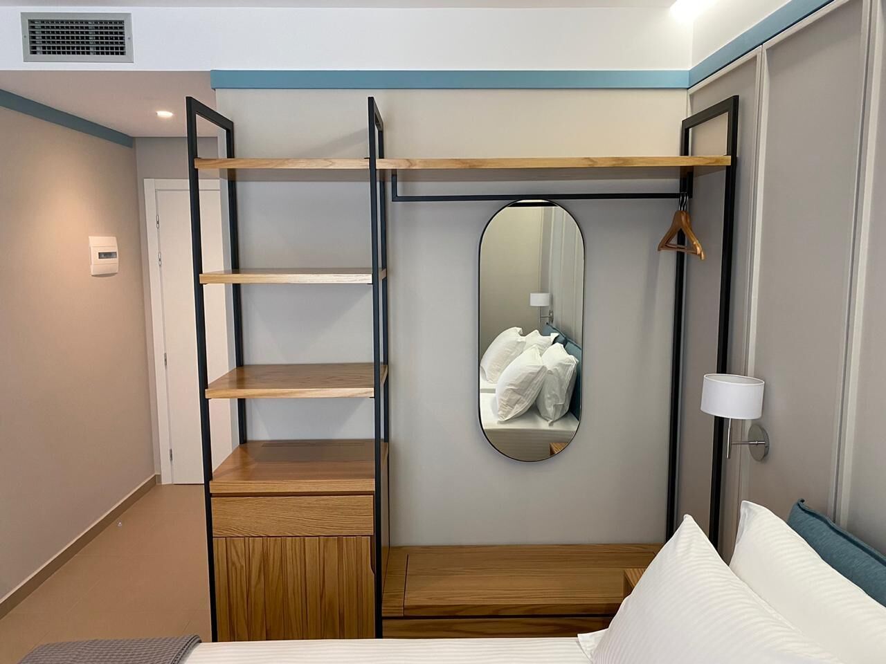 Een slaapkamer met een bed, een houten garderobe, een spiegel en een bedlampje.