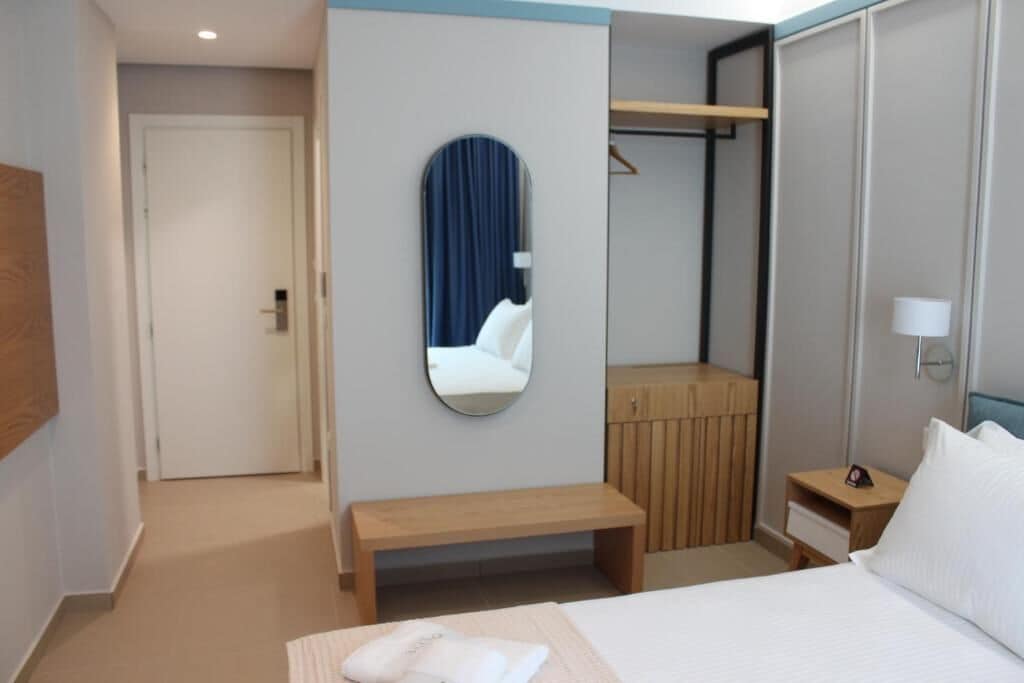 A hotel room with a bed, a bench, a mirror, a wardrobe, and a bedside table.