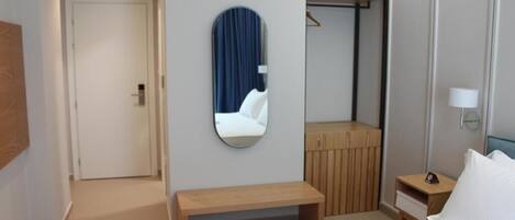 A hotel room with a bed, a bench, a mirror, a wardrobe, and a bedside table.