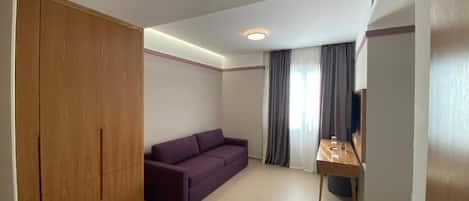 Ein Zimmer mit einem Holzschrank, einem violetten Sofa, einem kleinen Tisch mit einem Glas und einer Tür mit Griff.