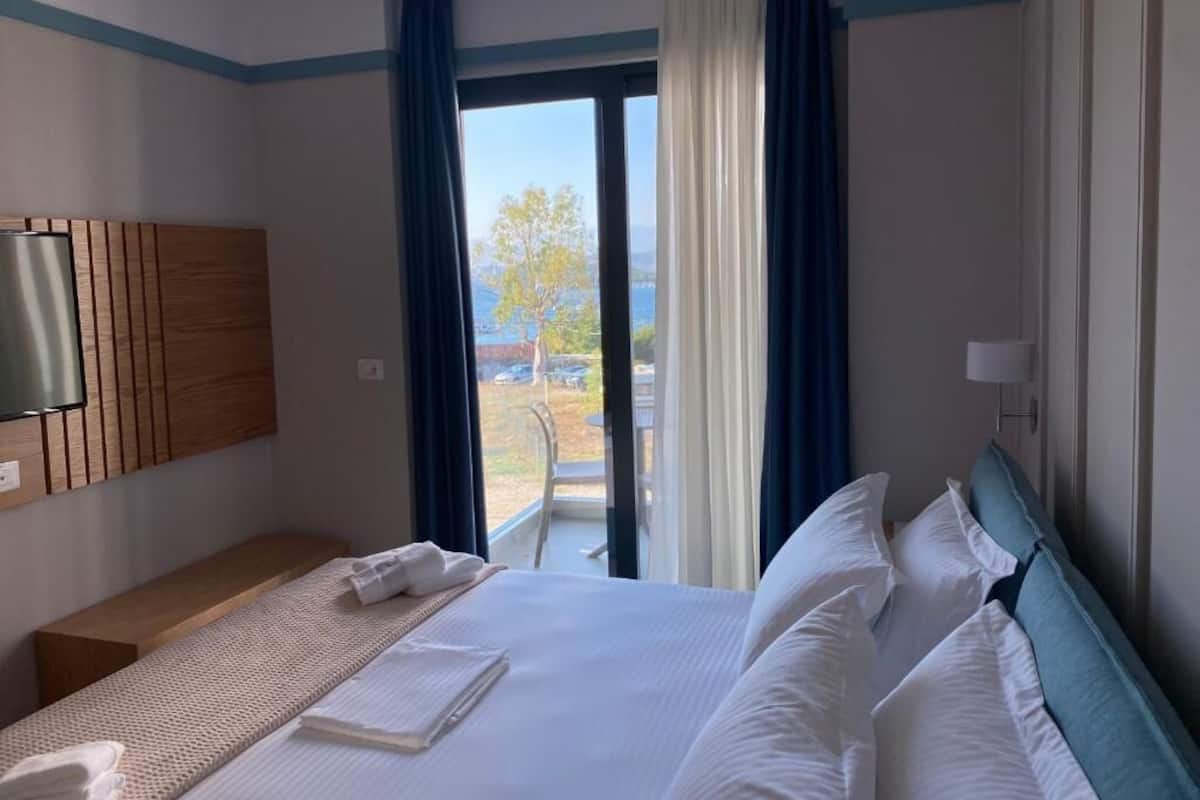 A hotel room with a bed, a TV mounted on the wall, and a view of the outdoors through a large window.