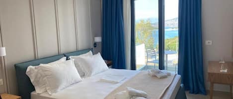 A hotel room with a large bed, a view of the sea, and a small table with a glass.