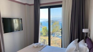 A hotel room with a bed, a TV mounted on the wall, and a view of the outdoors. - Olive Hotel Ksamil (Ksamil)