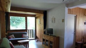 Uma sala de estar acolhedora com um sofá, uma TV sobre um móvel de madeira e uma porta que dá para uma área externa.