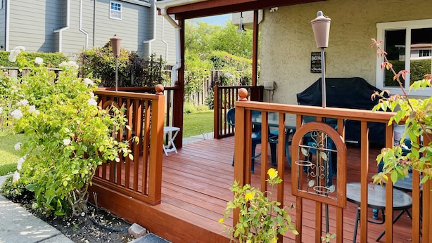 Una terraza de madera con un pérgola, mobiliario exterior y una zona de barbacoa.