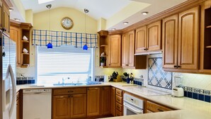 Una cocina con armarios de madera, horno empotrado, lavavajillas y una ventana con persianas.