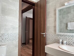 Features a spacious bathroom with a large mirror above a sink, mosaic tile border, and wooden floor.