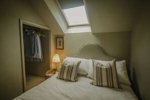 A bedroom with a skylight, a bed with striped pillows, a nightstand with a lamp, and a closet with hanging clothes. - Countryside views, Rural first floor cottage (Buxton)