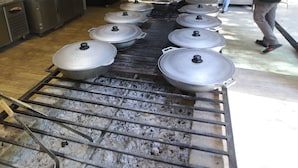 A kitchen with a long grill, pots on the grill, and people working. - Maajid Quba Hotel&Restaurant Sanatorium (Quba)