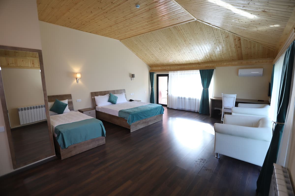 A room with two beds, a sofa, a radiator, and a window with curtains.