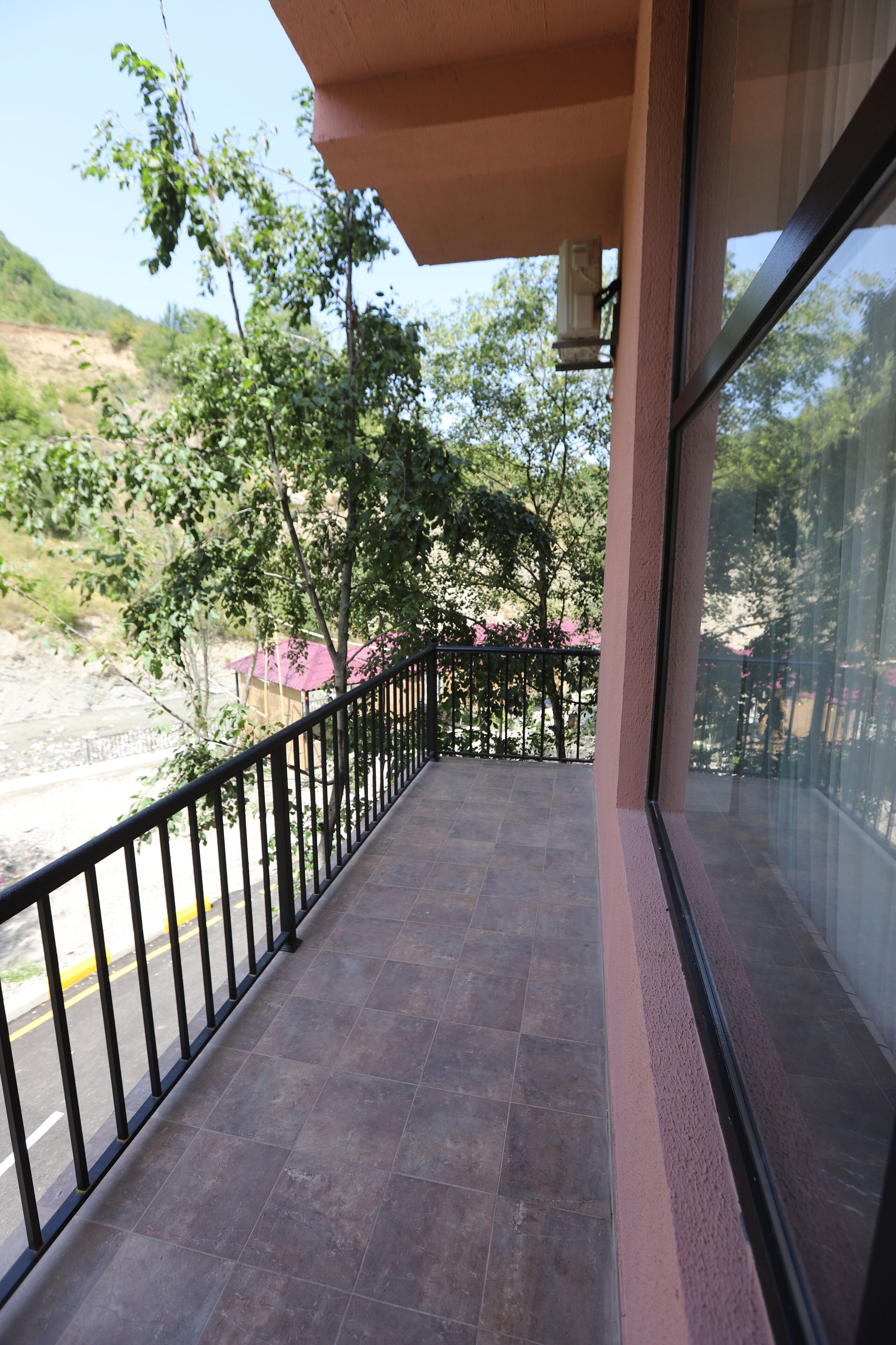 A balcony with a metal railing, a tiled floor, and a view of trees and a building in the background.