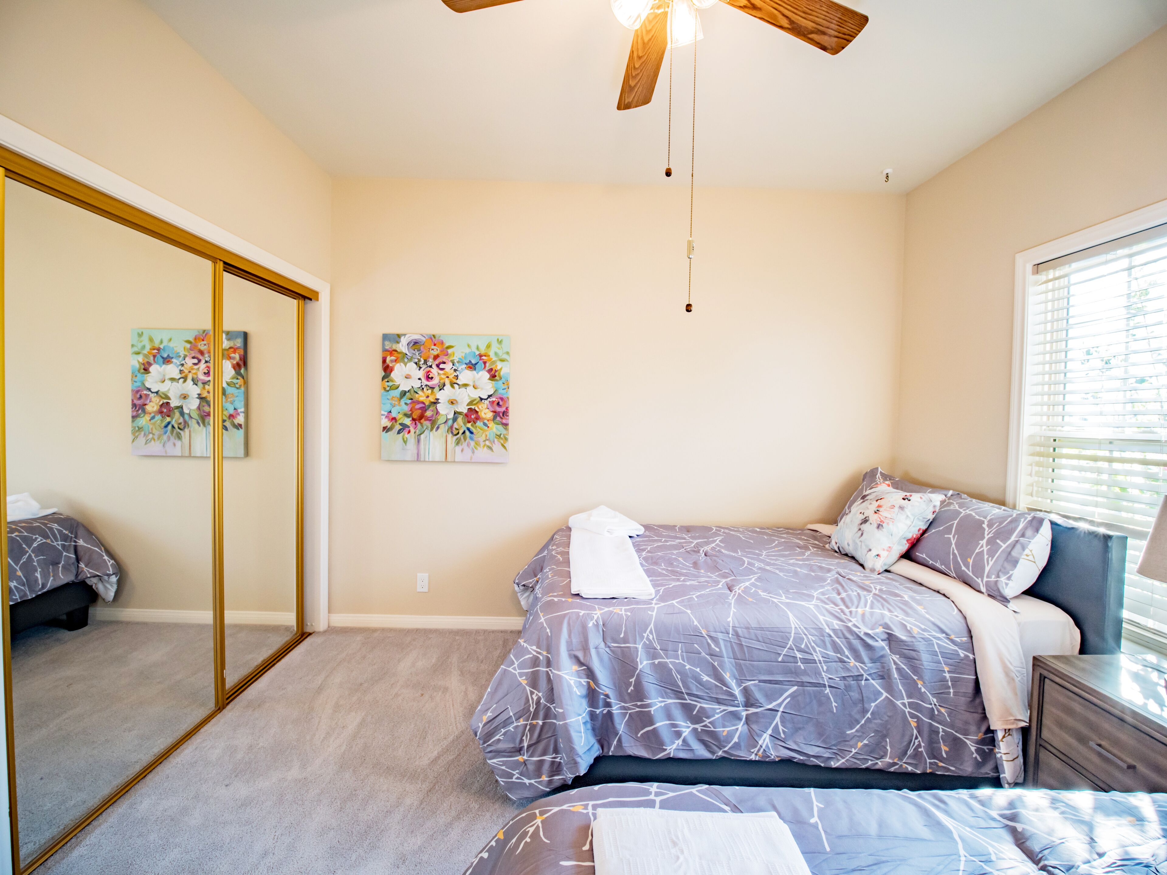 A bedroom with a bed, a dresser, a mirror, and two floral paintings on the wall.