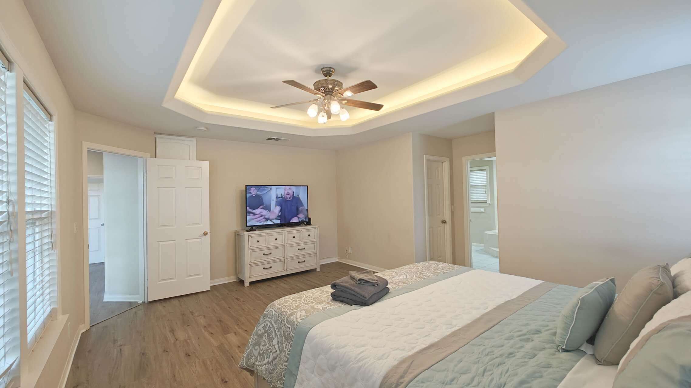 Une chambre à coucher avec un lit, un ventilateur de plafond, une télévision et une commode.