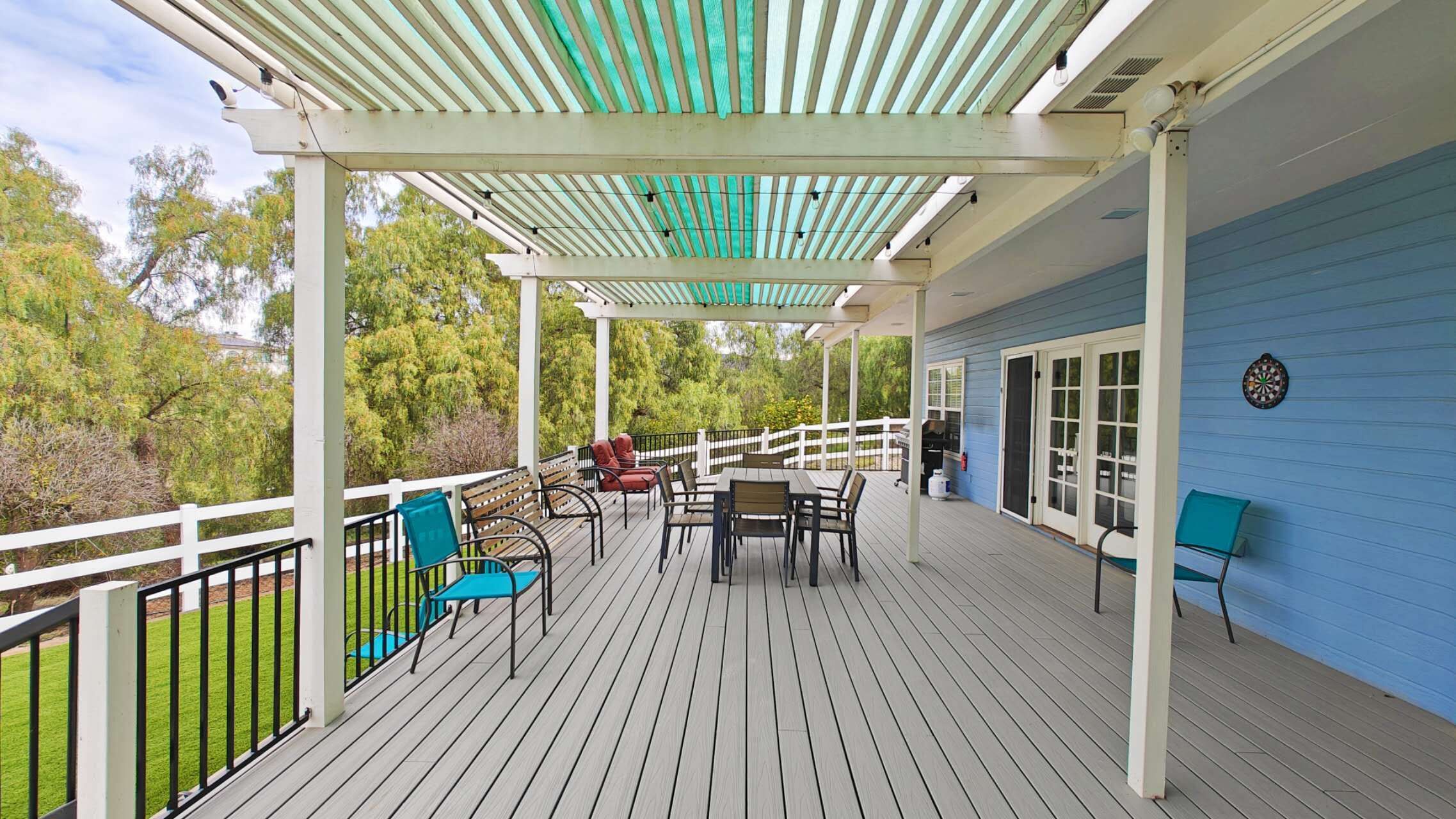 Une terrasse couverte, aménagée avec du mobilier d’extérieur, un barbecue et un jeu de fléchettes.