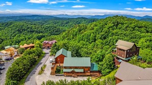 A lodge with multiple buildings surrounded by dense forest, a main building with a green roof, and a visible road. - Large Luxury Cabin Near Pigeon Forge | Indoor Pool, Theater, Sleeps 56 (Sevierville)