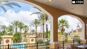 Un área de patio al aire libre con mesas y sillas, una piscina y palmeras.
